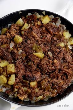 a skillet filled with meat and potatoes on top of a white countertop next to utensils