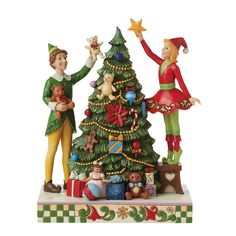 two figurines are standing next to a christmas tree with presents on the bottom