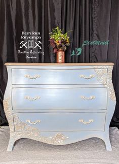 an antique dresser painted blue with gold trim and flowers on top, sits in front of a black curtain