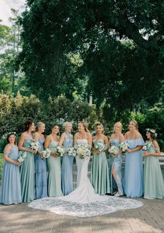 a group of women standing next to each other in front of trees and bushes with bouquets