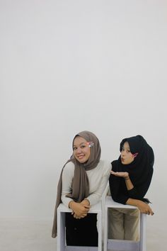 two women sitting on white chairs with one pointing at the camera while the other is holding her hand out