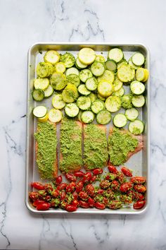 a tray filled with meat and vegetables on top of a marble countertop next to sliced cucumbers