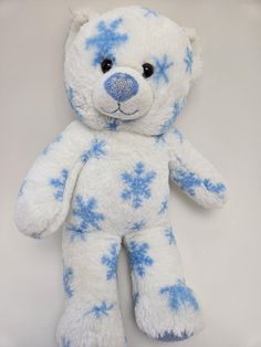 a white and blue teddy bear with snow flakes on it's face, sitting upright