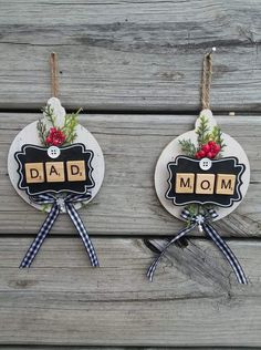 two christmas ornaments hanging on the side of a wooden fence with words and bows attached to them