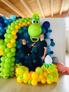 two people standing in front of a balloon arch with a green dragon head on it