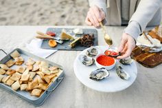 a woman is spooning some food from a plate on the beach with other foods