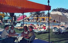 several people sitting at tables under umbrellas by the pool in an open air swimming area