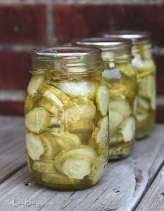 three mason jars filled with pickles sitting on top of a wooden table next to a brick wall