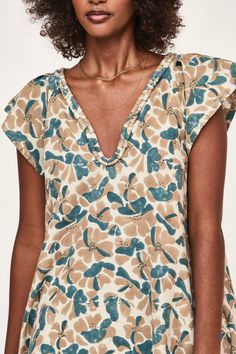 a woman with curly hair wearing a floral top and jeans, standing in front of a white background