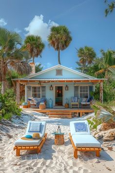 two chaise lounges on the beach in front of a house with palm trees