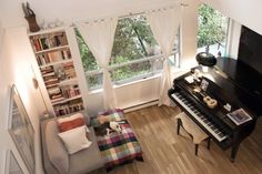 a living room filled with furniture and a piano in front of a large window next to a bookshelf