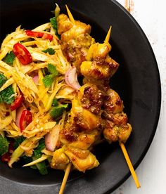 a black plate topped with meat and veggies next to chopsticks on a white table