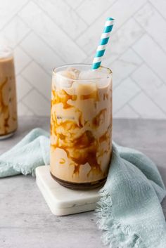 two glasses filled with iced coffee on top of a white marble counter next to blue and green striped straws