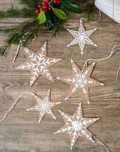 paper snowflakes are hanging from string on a wooden table with holly branches