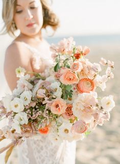 a woman holding a bouquet of flowers on the beach