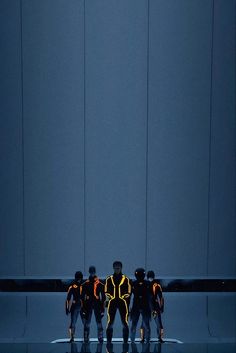 five people standing in front of a blue wall wearing black and yellow outfits with neon lights on them