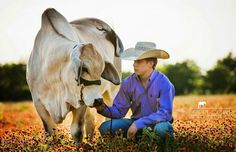 a man kneeling down next to a cow with a cowboy hat on it's head