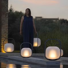 a woman is standing next to some lights in the water at sunset or dawn,