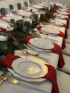 the table is set with white plates and silverware, red napkins and greenery