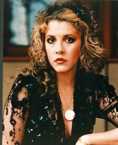 a woman with curly hair wearing a black dress and holding a white button in her left hand