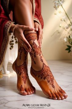 the legs and feet of a woman with henna tattoos on her body, in front of a flower arrangement