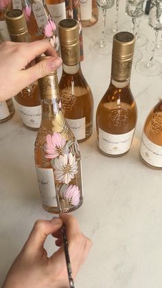 a person is writing on the label of a wine bottle with flowers painted on it