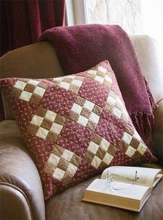 a brown couch with two pillows and a book on it next to a window sill