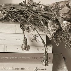 a bunch of books stacked on top of each other with dried flowers hanging from them