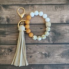 a tasseled bracelet with an egg and white bead on it, hanging from a gold plated charm