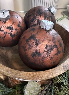 three brown ornaments in a wooden bowl on top of a table with greenery and rocks