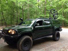 a green pick up truck with a bike on the roof parked in front of some trees