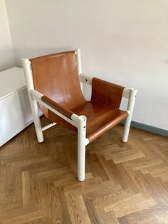 a brown leather chair sitting on top of a hard wood floor next to a white wall