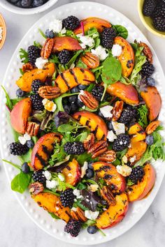 a salad with peaches, blackberries and pecans on a white platter