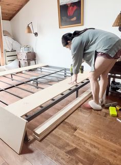 a woman is working on a bed frame in a room with hard wood flooring