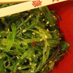 a red bowl filled with greens and chopsticks