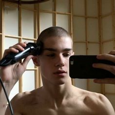 a shirtless man is holding a hair dryer and looking at his cell phone