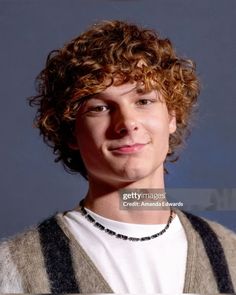 a young man with curly hair wearing a sweater and smiling at the camera stock photo