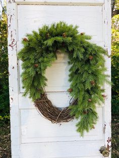 a wreath hanging on the side of a white door with pine cones and evergreen branches