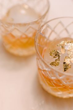 two glasses filled with liquid sitting on top of a white tablecloth covered table next to each other