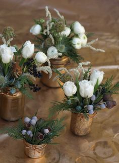 four small vases with flowers and greenery in them sitting on a gold table cloth