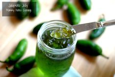 a jar filled with green liquid sitting on top of a wooden table next to peppers