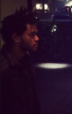 a man with dreadlocks standing in front of a building at night looking off into the distance