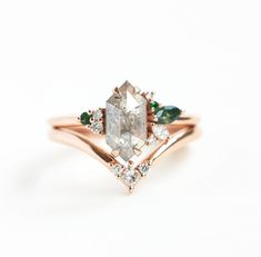 an engagement ring with two pear shaped diamonds and three emeralds on the band, set in 18k rose gold