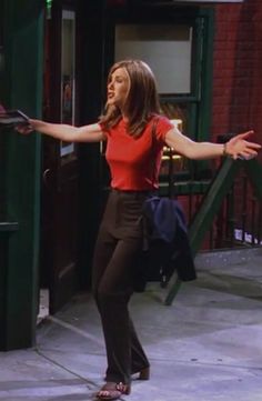 a woman in red shirt and black pants holding her arms out while standing on the sidewalk