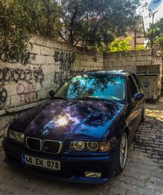 a blue car parked in front of a brick wall with graffiti on it's side