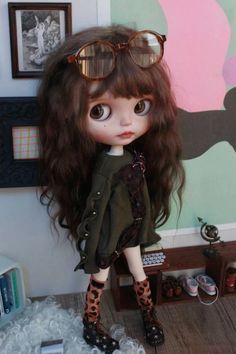 a doll with long hair and glasses on it's head standing in front of a wall