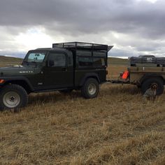 two jeeps pulling a trailer in a field