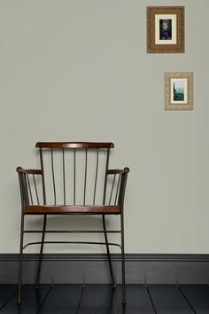 a wooden chair sitting in front of a wall with two pictures hanging on the wall