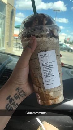 a person holding up a drink in front of a car with the words yummyminn written on it