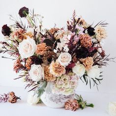 a vase filled with lots of flowers on top of a white table next to dried flowers